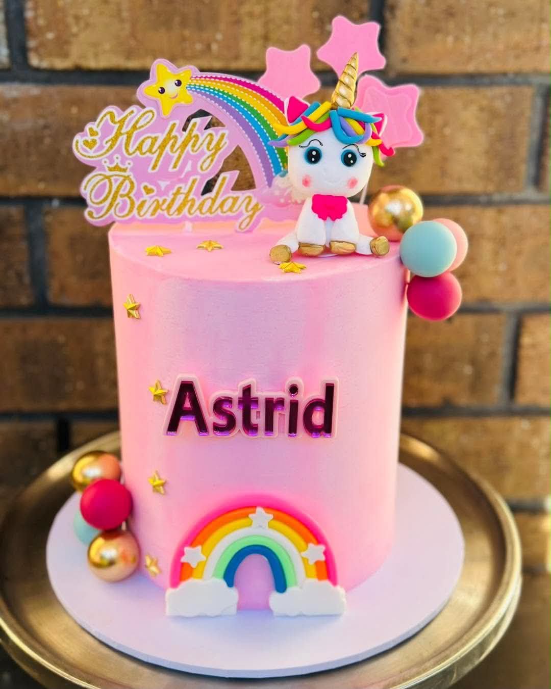 Pink unicorn birthday cake with rainbow topper and gold star decorations for Astrid